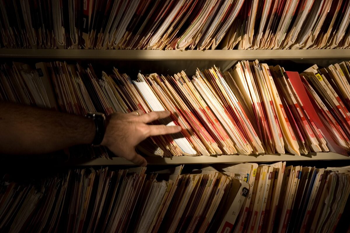 A man in front of a bookshelf of medical records